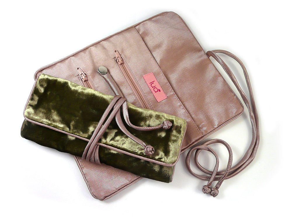 A blush pink silky lined jewellery roll with a matching strap, shown open to reveal interior zip compartments, alongside a matching olive green velvet rolled jewellery holder tied with the same strap, on a white background.