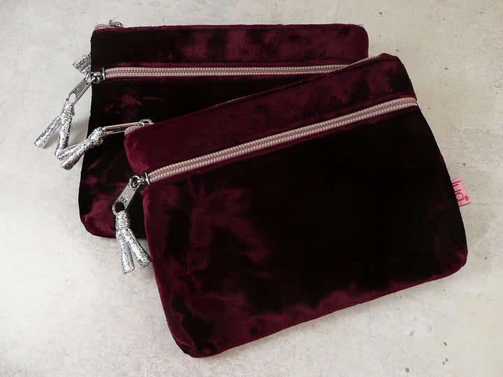 Two burgundy velvet zipped pouches with metallic silver ties, displayed on a light textured surface.