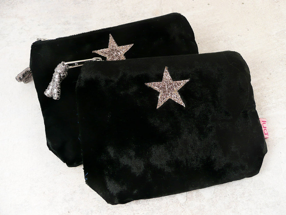 Two black velvet purses with an appliquéd star on a concrete background.