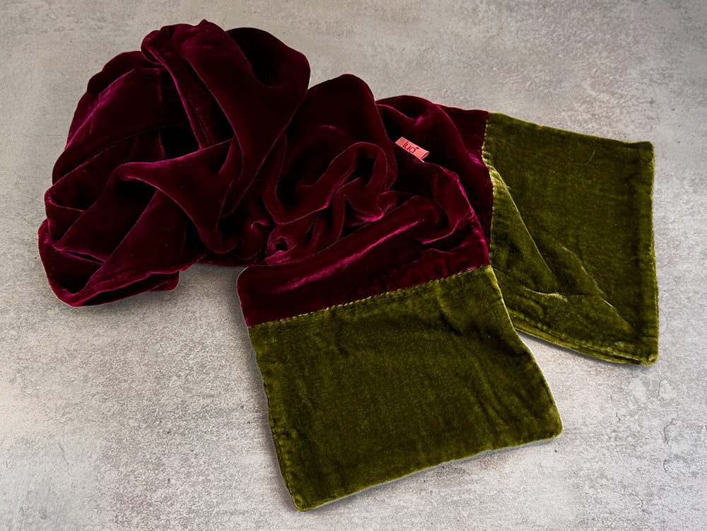 A plush velvet throw blanket with a deep burgundy top section and an olive green bottom section, styled in a crumpled flat-lay on a textured grey concrete surface.