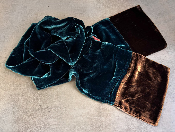 A velvet scarf with a colour-blocked design, featuring a teal green section and a dark brown section, shown on a textured grey background.