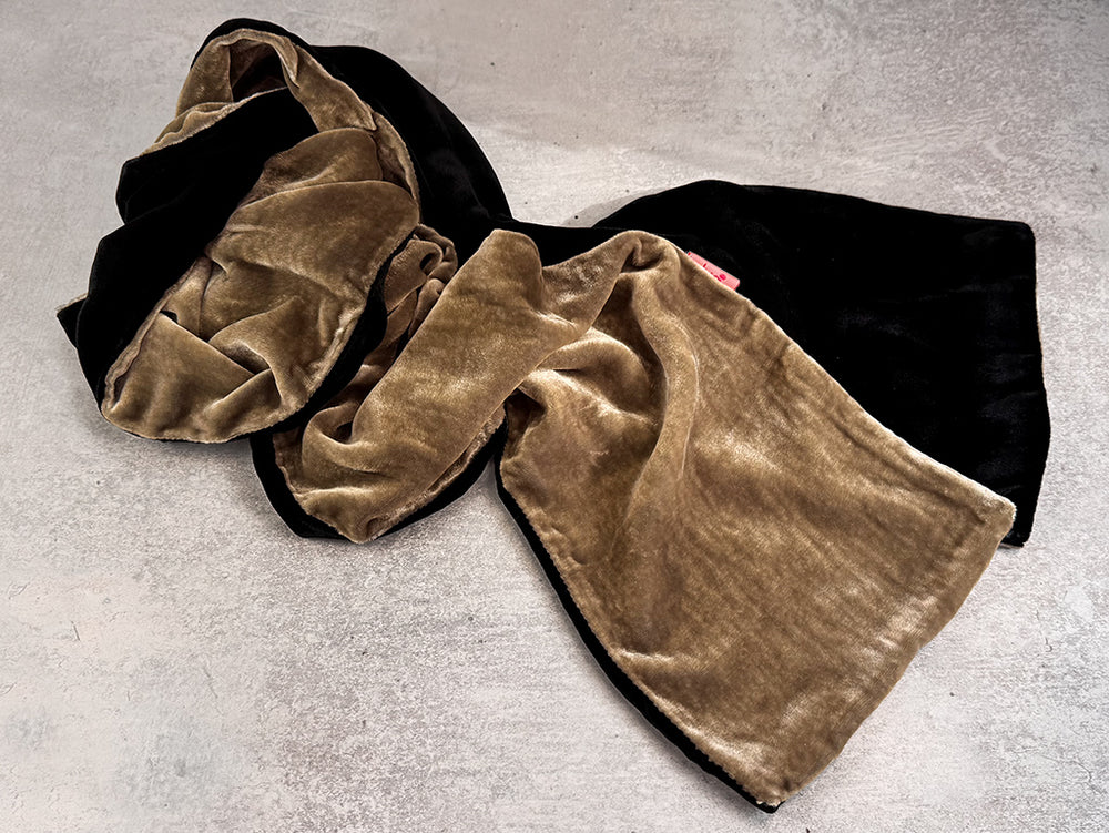 A plush velvet scarf in black and tan, draped on a textured gray concrete surface.