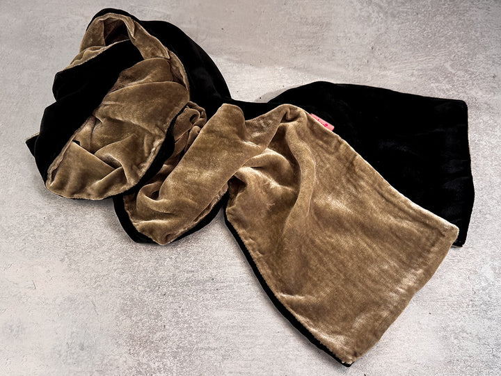 A plush velvet scarf in black and tan, draped on a textured gray concrete surface.