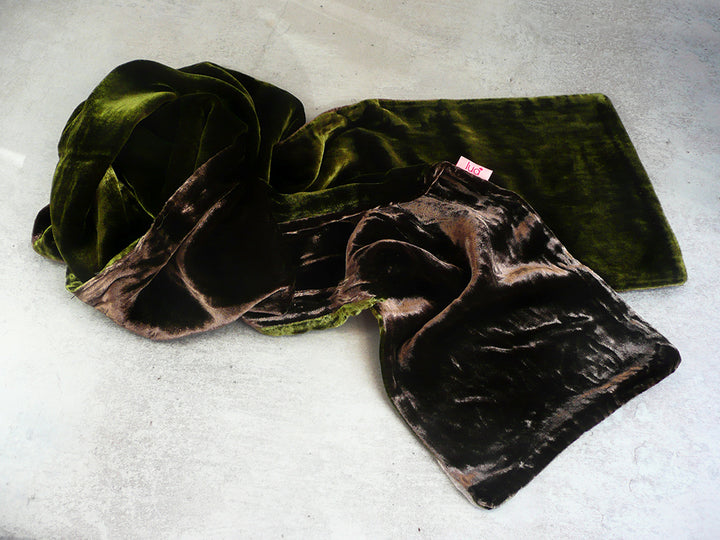 A dark green velvet scarf with a brown and black mottled patterned reverse side, laid out on a light gray textured surface.