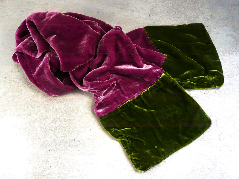 A plush velvet scarf in a colour-blocked design, featuring a magenta-purple section and an olive green section, shown on a grey textured background.